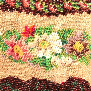 May include: A close-up of a beaded purse with a floral design. The purse is made of brown, green, white, pink, and yellow beads. The beads are arranged in a pattern of flowers and leaves.
