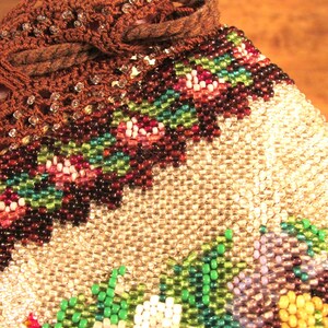 May include: A beaded bag with a brown crocheted top and a floral design. The bag is made with small, iridescent beads in shades of white, green, purple, and yellow.