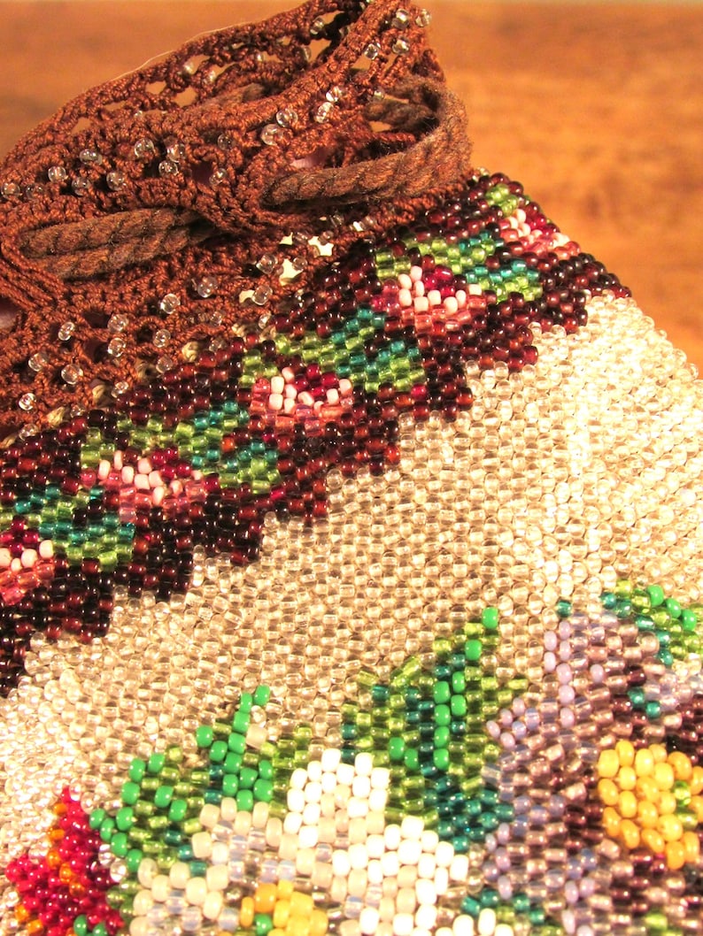 May include: A beaded bag with a brown crocheted top and a floral design. The bag is made with small, iridescent beads in shades of white, green, purple, and yellow.