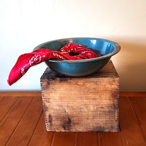 May include: A vintage teal blue enamelware bowl with a red bandana inside, sitting on a wooden crate.