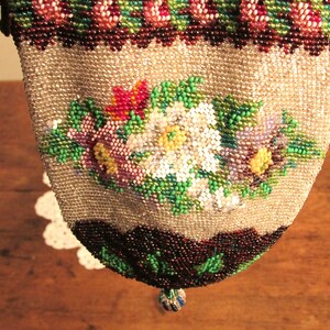 May include: A beaded purse with a floral design in shades of pink, white, green, and purple. The purse is made of small, iridescent beads and has a drawstring closure.
