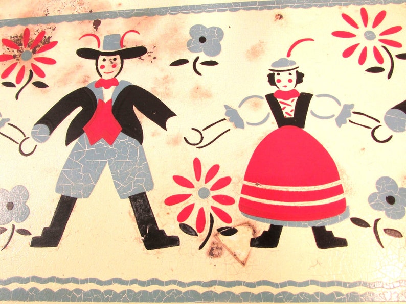 Puede incluir: Una fiambrera vintage de hojalata con un dise&ntilde;o pintado de dos figuras en trajes tradicionales folcl&oacute;ricos bailando. Las figuras est&aacute;n rodeadas de flores estilizadas en rojo, azul y blanco.