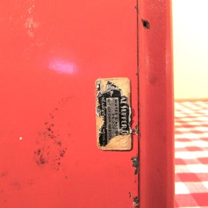 Puede incluir: Una caja de metal roja con una pegatina blanca que dice "AL SUPPERI WATER-PROOF OIL-PROOF MADE IN CHICAGO, ILL."