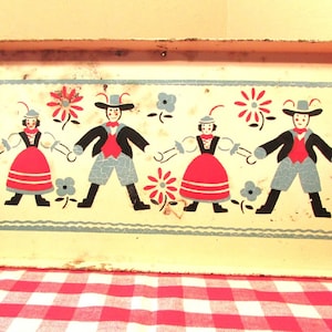 Puede incluir: Una bandeja de metal vintage con borde rojo e interior blanco. La bandeja presenta un dise&ntilde;o colorido de cuatro figuras con ropa tradicional, bailando y tom&aacute;ndose de la mano. Las figuras est&aacute;n rodeadas de flores y hojas.