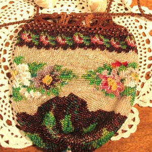 May include: A vintage beaded purse with a floral design in shades of pink, green, and brown. The purse has a drawstring closure and a brown crocheted top.
