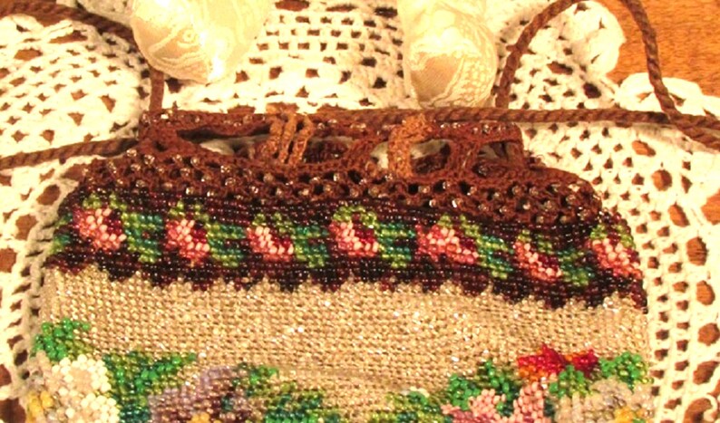 May include: A beaded purse with a brown crocheted top and floral design. The purse has a drawstring closure and a long brown cord.