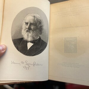 以下が含まれることがあります： アメリカの詩人、ヘンリー・ワズワース・ロングフェローの白黒肖像画。本の中に「ヘンリー・W・ロングフェロー 1879」という手書きの署名があります。