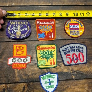 May include: Seven vintage bowling patches with various designs and colors. The patches feature text such as "WIBC League Champion", "Brunswick 500 Series", "ABC American Bowling Congress", "600 Series", "500 Club", and "WIBC Seattle 1980".