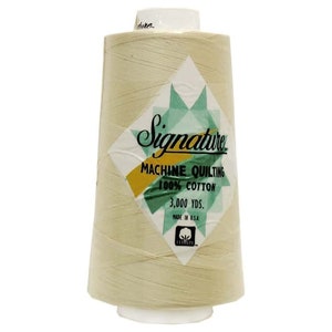 May include: A spool of Signature machine quilting thread, 100% cotton, in a light beige color. The label features a geometric design with the text "Signature Machine Quilting 100% Cotton 3,000 YDS. Made in U.S.A."
