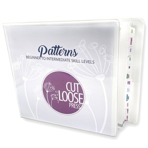 May include: A clear, three-ring binder with a cover featuring the word "Patterns" in a script font, with "Beginner to Intermediate Skill Levels" below. A purple circle with "Cut Loose Press" is also on the cover. Labeled dividers are visible.