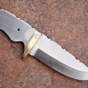 May include: A silver knife with a brass handle and a serrated edge. The knife has a curved blade and a small hole in the handle.