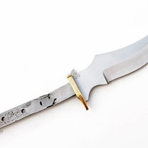 May include: A silver knife blade with a curved edge and a brass tang. The blade is about 7 inches long.