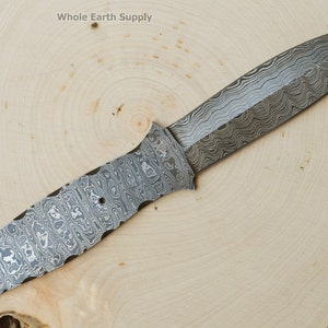Peut inclure: Une lame de couteau en acier Damas avec une pointe pointue et un motif texturé. La lame mesure environ 25 cm de long et possède un manche avec un motif similaire.