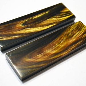 May include: Two rectangular pieces of black and gold marbled resin, likely for crafting or making handles.