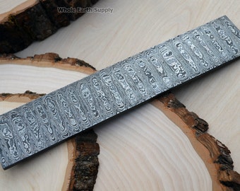 May include: A close-up of a long, rectangular piece of steel with a wavy, patterned surface. The steel is a light grey colour with a subtle sheen. The steel is lying on a wooden surface.