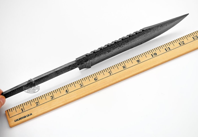 K&ouml;nnte beinhalten: Eine schwarze Stahlmesserklinge mit strukturierter Oberfl&auml;che und einer scharfen Spitze. Die Klinge wird an einem Holzlineal gemessen und ist 30,5 cm lang.