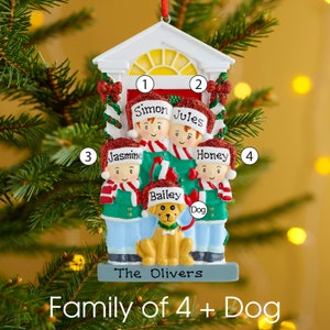 K&ouml;nnte beinhalten: Ein Weihnachtsbaumschmuck in Form eines Hauseingangs mit vier Figuren, die rote Weihnachtsm&uuml;tzen und gr&uuml;ne Jacken mit rot-wei&szlig; gestreiften Schals tragen. Die Namen Simon, Jules, Jasmine, Honey und Bailey sind auf den M&uuml;tzen aufgedruckt.