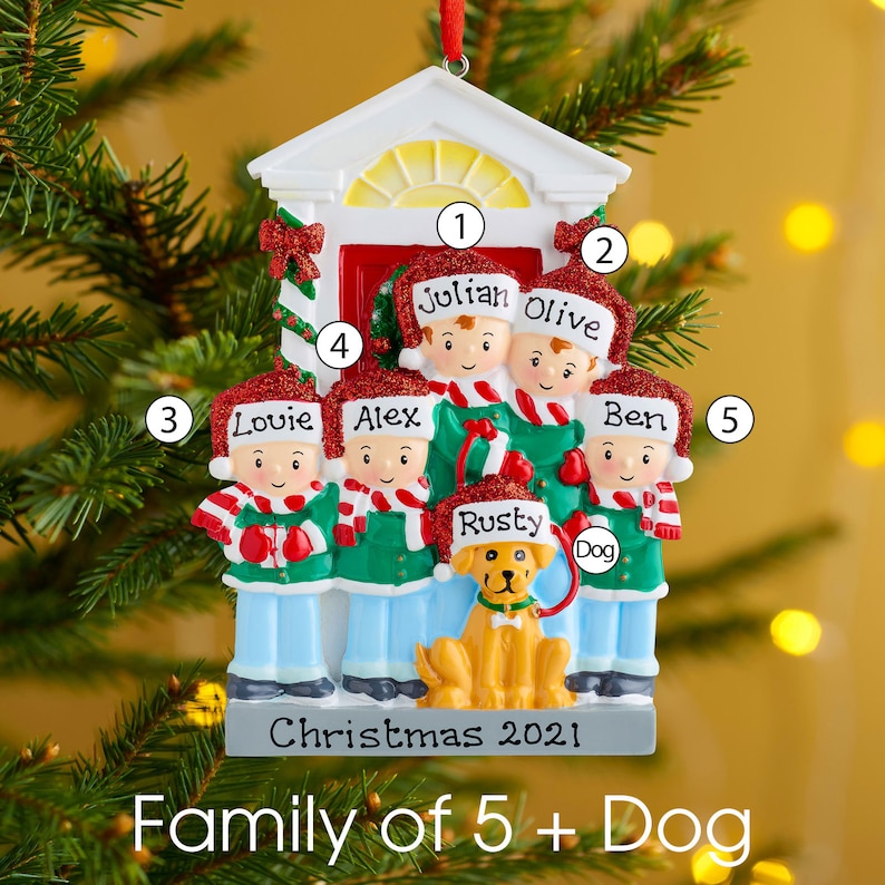 K&ouml;nnte beinhalten: Ein personalisierter Weihnachtsbaumschmuck mit f&uuml;nf Figuren und einem Hund vor einem wei&szlig;en T&uuml;rrahmen. Jede Figur tr&auml;gt eine rote, glitzernde Weihnachtsm&uuml;tze mit einem darauf geschriebenen Namen: Julian, Olive, Louie, Alex, Ben und der Hund Rusty.