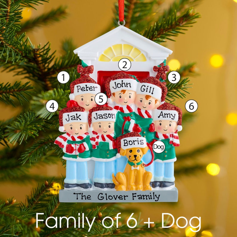 K&ouml;nnte beinhalten: Ein personalisierter Weihnachtsbaumschmuck mit einer sechsk&ouml;pfigen Familie und einem Hund vor einer Hausfassade. Jede Figur tr&auml;gt eine rote Glitzerm&uuml;tze mit einem darauf geschriebenen Namen, darunter Peter, John, Gill, Jak, Jason, Amy und Boris.