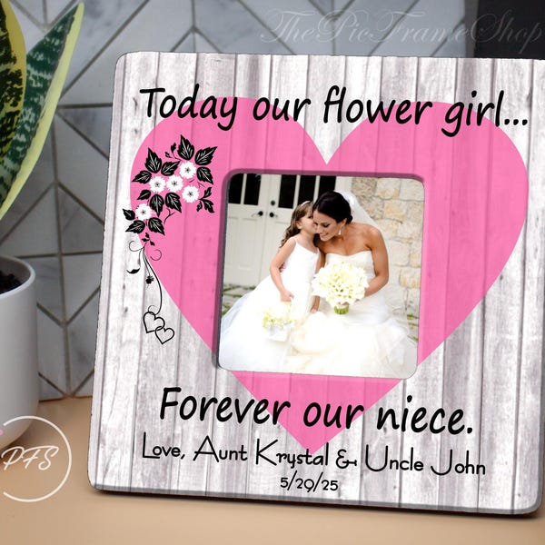 May include: A white wooden picture frame with a pink heart shape in the center. The frame has the text "Today our flower girl... Forever our niece. Love, Aunt Krystal & Uncle John 5/29/25" printed on it.