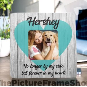 Pode incluir: Uma moldura de madeira com um padr&atilde;o de gr&atilde;o de madeira cinza claro. A moldura tem uma forma de cora&ccedil;&atilde;o turquesa com uma foto de uma mulher e um c&atilde;o golden retriever dentro. O texto "Hershey" est&aacute; no topo da moldura e o texto "No longer by my side but forever in my heart" est&aacute; na parte inferior.