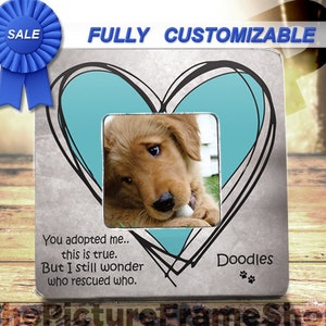 May include: A silver picture frame with a blue heart design and a photo of a golden retriever puppy. The frame has the text "You adopted me... this is true. But I still wonder who rescued who." and "Doodles" with paw prints.