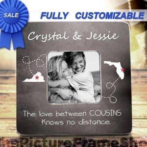 May include: A gray picture frame with a black and white photo of two women hugging. The frame has a white border and a black background with the text "Crystal & Jessie" and "The love between COUSINS Knows no distance". There are two red stars on the frame, one next to the outline of Virginia and the other next to the outline of Florida.