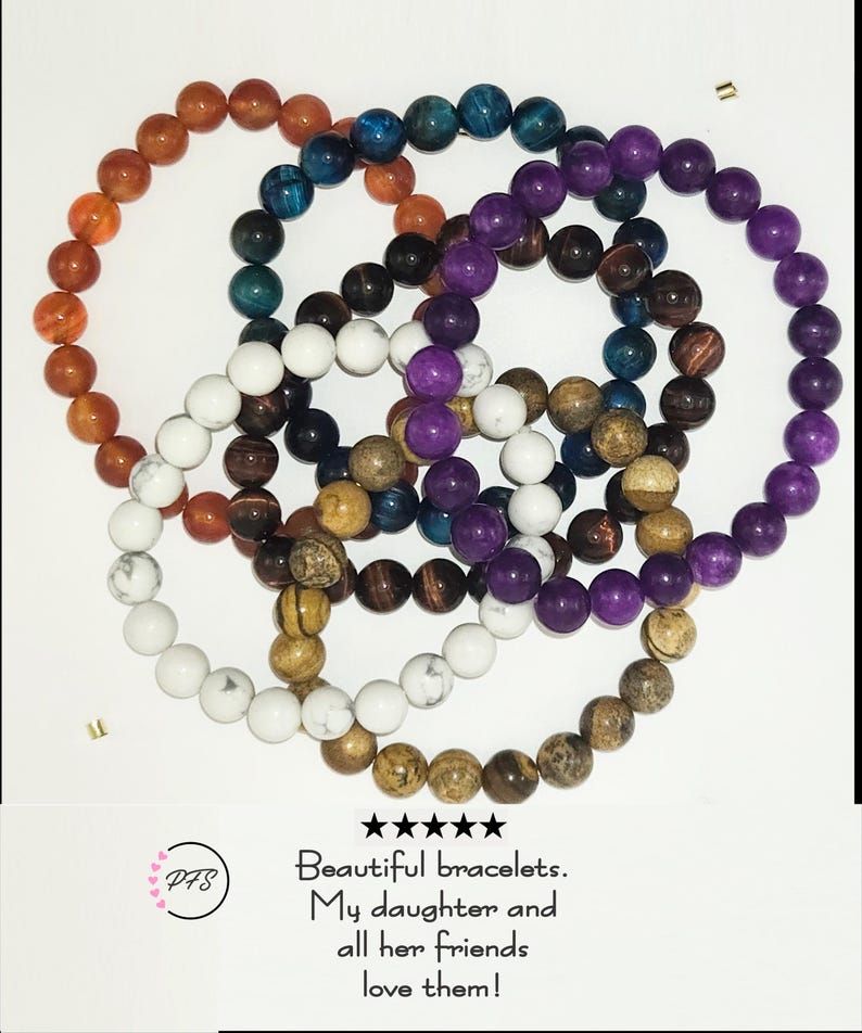 Op de afbeelding: Een collectie van vijf ronde kralenarmbanden met gladde, ronde stenen in diverse kleuren, waaronder oranje, blauw, paars, wit en bruin. Onder de armbanden staat de tekst: 5 sterren, Beautiful bracelets. My daughter and all her friends love them!