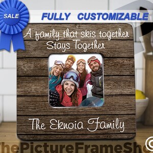 May include: A wooden picture frame with a rustic woodgrain design. The frame has a white inscription that reads "A family that skis together stays together." The frame also has a smaller picture frame inside with a photo of a family of skiers. The inscription at the bottom reads "The Eknoia Family."