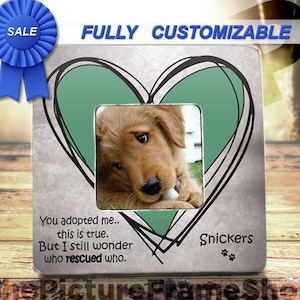 May include: A silver metal picture frame with a green heart design and a photo of a golden retriever puppy. The frame has the text "You adopted me... this is true. But I still wonder who rescued who." and "Snickers" with paw prints.