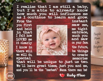 Könnte beinhalten: Ein quadratischer Bilderrahmen mit dunkelrotem Holzmaserungshintergrund und weißem Text, der an eine Nana gerichtet ist. In der Mitte befindet sich ein Foto eines lächelnden Babys mit einem rosa Schleifen-Stirnband. Der Name Ruby Mae steht unten.