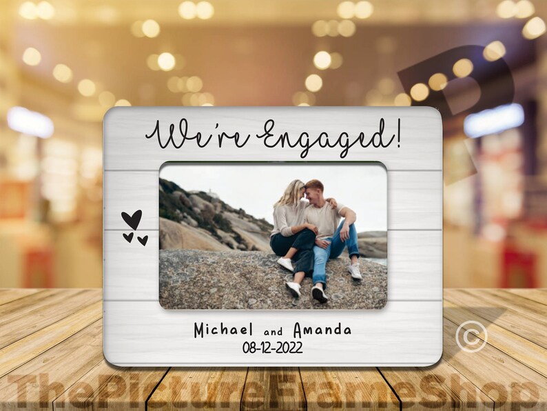 May include: White wooden photo frame with the text "We're Engaged!" and a photo of a couple. The frame also includes the names "Michael and Amanda" and the date "08-12-2022".