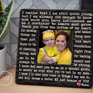 May include: A black wood picture frame with a white inscription and a photo of a child and adult dressed in yellow. The inscription reads "I realize that I am still quite young, but I am already old enough to know how much you have influenced me as I continue to learn and grow. Thank you from the bottom of my heart, for knowing focus on than just Thanks for the of discerning wrong, and me to be always to "book"smart. foundation right from for teaching myself and be strong. I know God sent you to me as a special guide, to mentor me even when you're not by my side. I know I'll hear your voice in things I say and do, and will become a better ME just because of YOU! Reese"