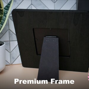 Peut inclure: Cadre photo en bois noir avec un support noir. Le cadre est pos&eacute; sur une surface brun clair. "Premium Frame" est &eacute;crit en blanc sous le cadre.