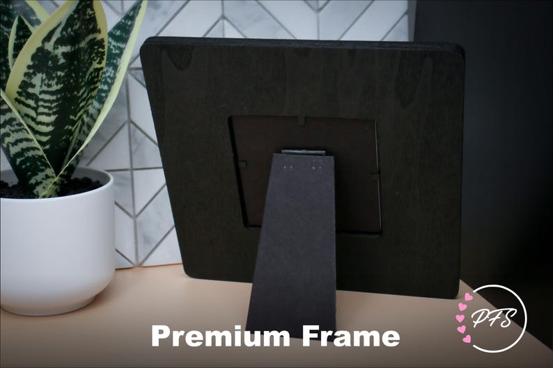 Peut inclure: Cadre photo en bois noir avec un support noir. Le cadre est pos&eacute; sur une surface brun clair. "Premium Frame" est &eacute;crit en blanc sous le cadre.
