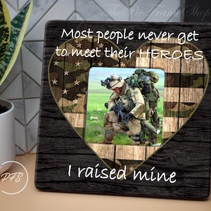 May include: A black wooden heart-shaped picture frame with a camouflage and American flag design. The frame has the text "Most people never get to meet their HEROES I raised mine".