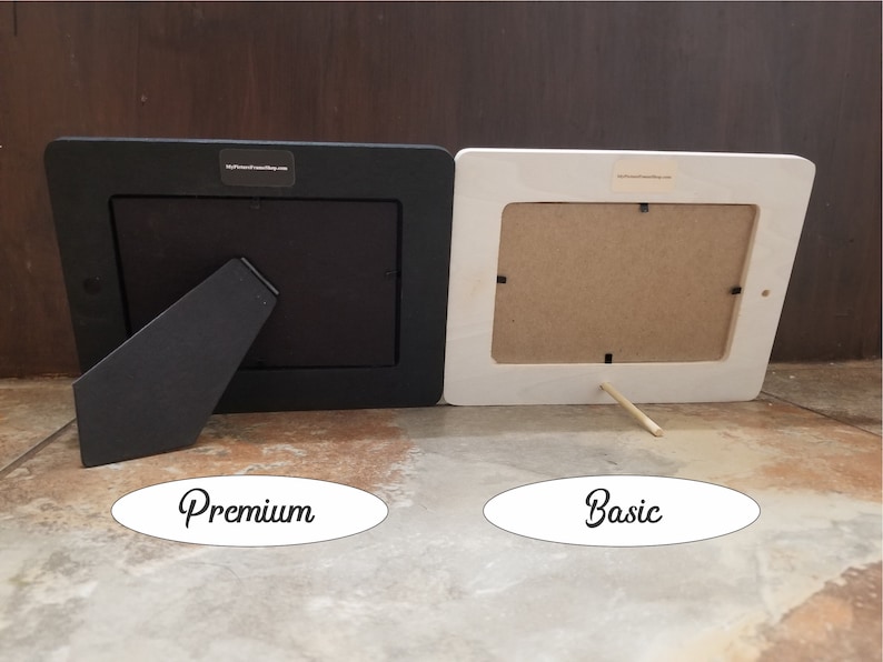 May include: Two picture frames, one black and one white, are shown from the back. The black frame has a black kickstand and the white frame has a wooden kickstand. The black frame is labelled "Premium" and the white frame is labelled "Basic".