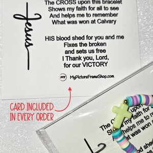 Op de afbeelding: Een armband van veelkleurige kleikralen met een lichtgroene kruisbedel, verpakt in een doorzichtige plastic hoes met een informatiekaart. De kaart toont de tekst: The CROSS upon this bracelet Shows my faith for all to see.