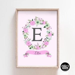 May include: A pink floral wreath with a gray letter E in the center. A pink banner with the name "Ella" is below the wreath.