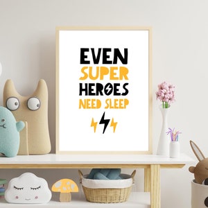 May include: A white framed print with black and yellow text that reads "Even Super Heroes Need Sleep" with two yellow lightning bolts underneath. The print is on a shelf with a variety of toys and decor.