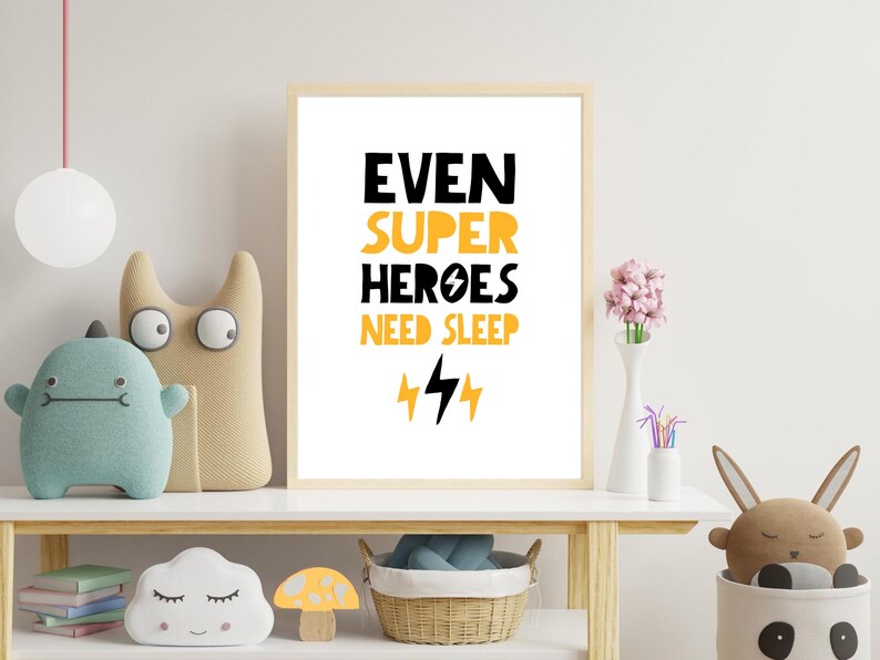 May include: A white framed print with black and yellow text that reads "Even Super Heroes Need Sleep" with two yellow lightning bolts underneath. The print is on a shelf with a variety of toys and decor.