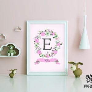 May include: A printable nursery art print with a pink background featuring a floral wreath with the letter E in the center and the name Ella written on a pink ribbon banner below the wreath.