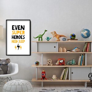 May include: A white framed poster with black and yellow text that reads "Even Super Heroes Need Sleep" with two yellow lightning bolts underneath. The poster is hanging on a white wall above a wooden shelf with a globe, dinosaur toys, and books.