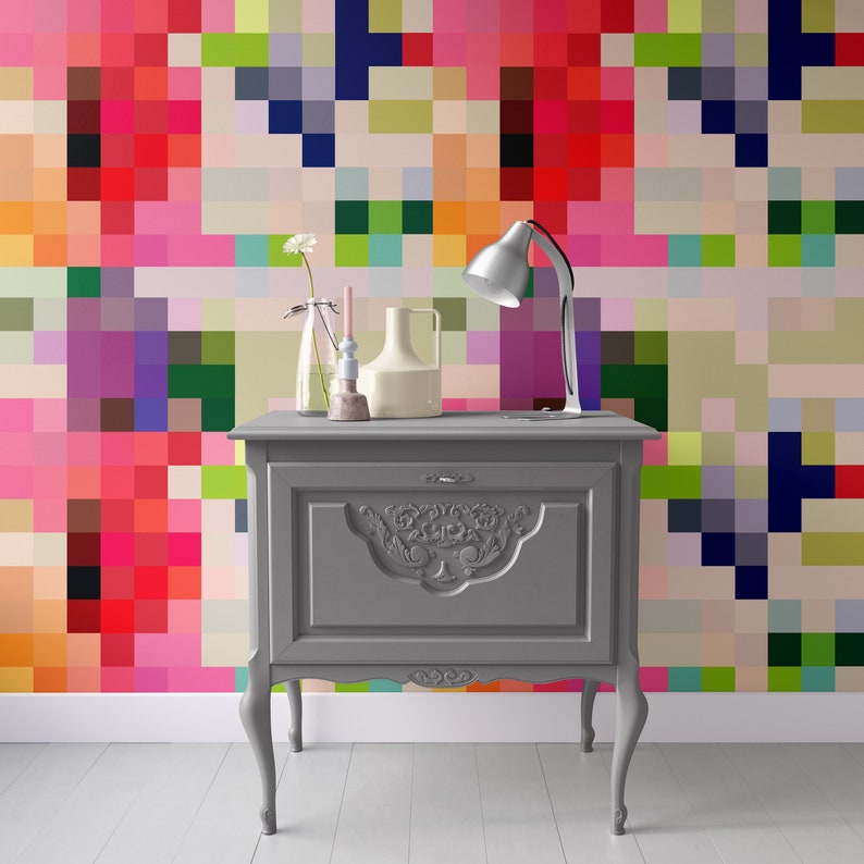 Puede incluir: Un armario de madera gris con tallas ornamentadas y un solo caj&oacute;n. El armario est&aacute; delante de una pared con un patr&oacute;n pixelado de colores.