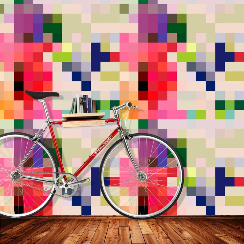 Puede incluir: Una bicicleta roja con un estante de madera sujeto al manillar. El estante tiene una pila de libros. La bicicleta est&aacute; delante de una pared con un patr&oacute;n pixelado de colores.