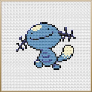 May include: A cross-stitch of a blue cartoon creature with a light blue body, dark blue accents, and a cream-colored tail. The creature has a smiling face and is set against a white background within a gold-colored frame.