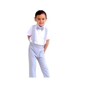 May include: A young boy wearing a white shirt with a gray bow tie and matching gray pants with suspenders.