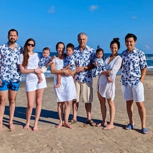 K&ouml;nnte beinhalten: Eine achtk&ouml;pfige Familie in passenden blau-wei&szlig;en gemusterten Hemden und Kleidern posiert an einem Sandstrand. Die Erwachsenen tragen Khaki-Shorts und die Kinder wei&szlig;e Shorts. Die Familie l&auml;chelt und schaut in die Kamera.
