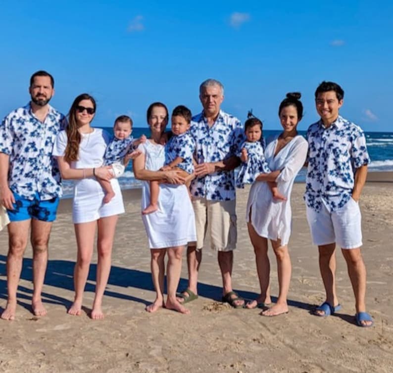 K&ouml;nnte beinhalten: Eine achtk&ouml;pfige Familie in passenden blau-wei&szlig;en gemusterten Hemden und Kleidern posiert an einem Sandstrand. Die Erwachsenen tragen Khaki-Shorts und die Kinder wei&szlig;e Shorts. Die Familie l&auml;chelt und schaut in die Kamera.