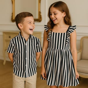 Op de afbeelding: Een jongen en een meisje lachen, beiden gekleed in bijpassende zwart-wit gestreepte outfits. De jongen draagt een shirt met korte mouwen en een beige korte broek. Het meisje draagt een mouwloze jurk met ruches.
